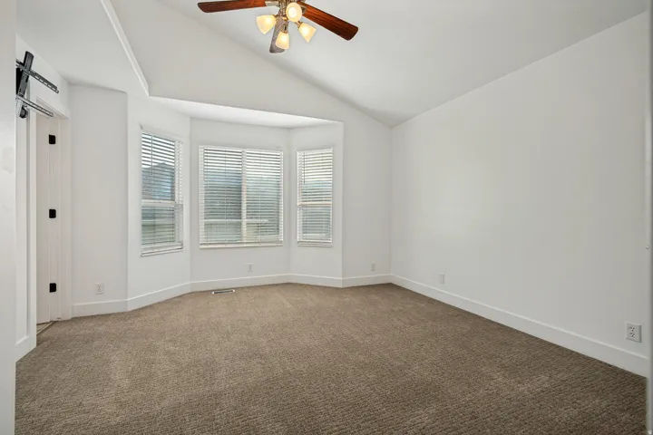 Vaulted ceiling with an attached ceiling fan, bay window with blinds, and neutral carpet flooring
