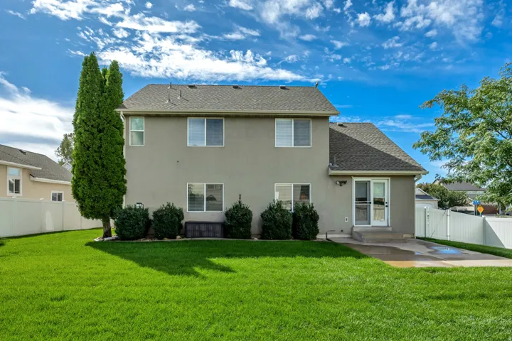 Two-story stucco exterior with a gabled roof, rear patio, sliding glass door, and a white privacy fence