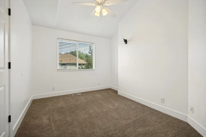 Carpeted room with a window featuring blinds, a ceiling fan with light, and vaulted ceilings