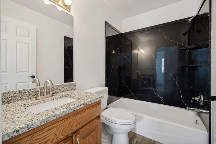 White paneled door, wood-finish vanity with an integrated sink, brushed nickel faucet, light speckled countertop, and a white toilet