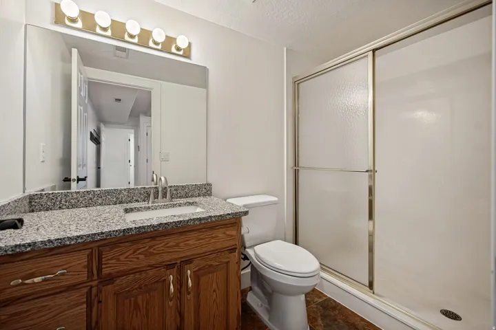Granite-style countertop with integrated sink, wood-finish vanity with cabinet storage, brushed nickel faucet, and a shower with sliding frosted glass doors