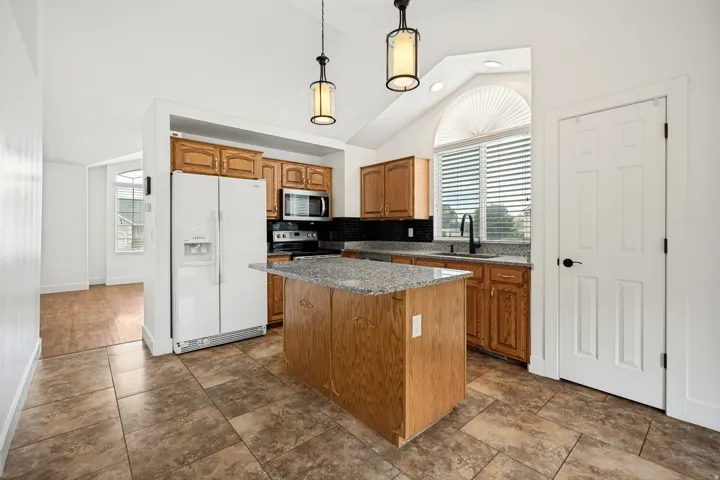 Kitchen featuring wood cabinetry, a center island with a stone-finish countertop, tile flooring, and a vaulted ceiling with pendant lighting
