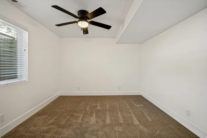 Carpeted room featuring a ceiling fan with integrated lighting, a window with horizontal blinds, and a dropped ceiling section