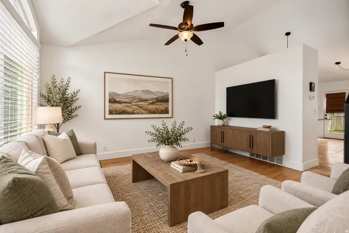 Virtually staged:Vaulted ceiling with a ceiling fan, large windows with blinds, wood-finish flooring, a built-in media console, and a partial wall element