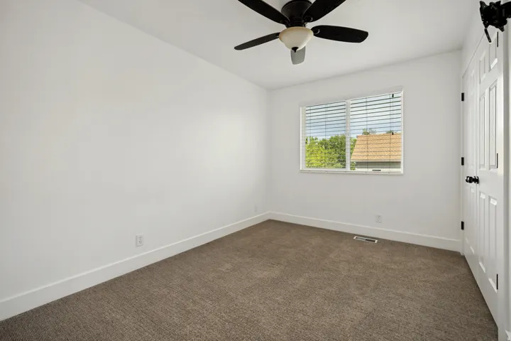 Brown carpet flooring, white walls, ceiling fan, white paneled door, and a single window with horizontal blinds