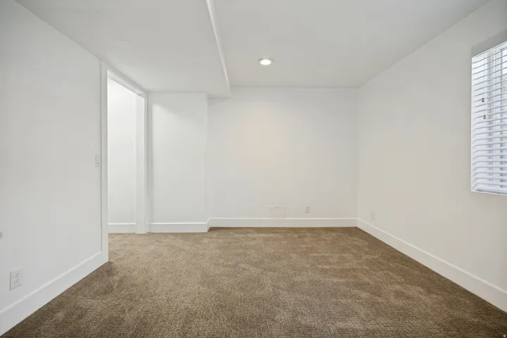 Recessed lighting, window with blinds, neutral carpet, white baseboards, and a doorway