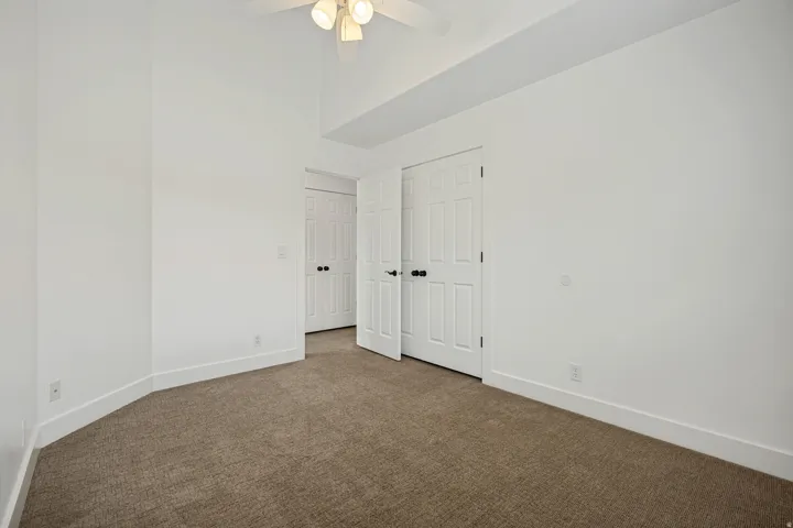 Vaulted ceiling with a ceiling fan, white paneled doors, and neutral carpet flooring