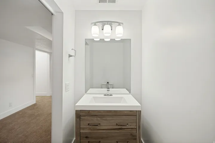 White vanity with integrated sink, wood-finish cabinetry, and chrome fixtures