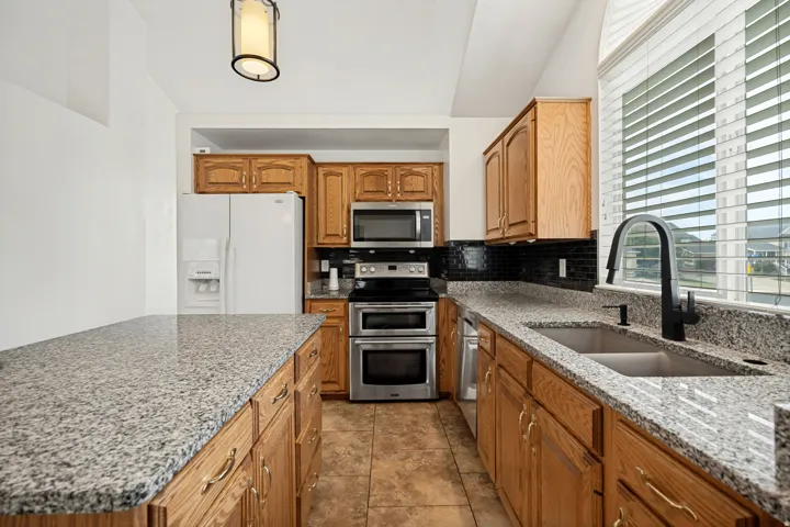 Kitchen featuring wood cabinetry, granite-finish countertops, stainless steel appliances, and a double basin sink with a matte black faucet