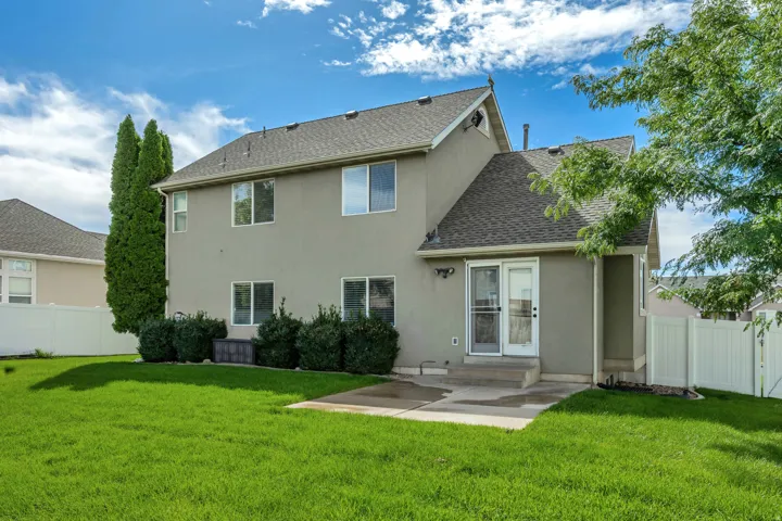 Expansive green lawn, stucco exterior, multiple windows, sliding glass door, and a white privacy fence