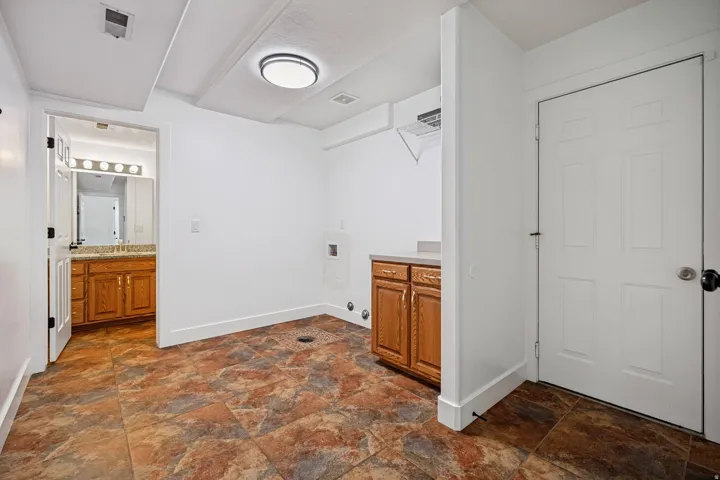 Utility space with patterned floor tiling, wood-finish cabinetry, and overhead lighting