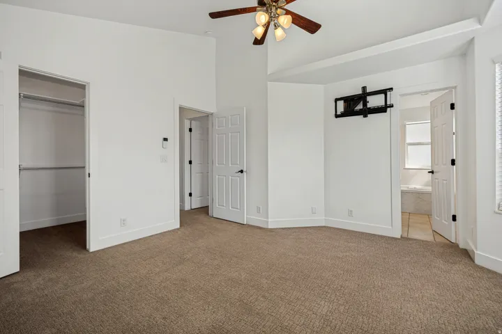 Vaulted ceiling, ceiling fan with integrated lighting, wall-mounted television bracket, built-in closet with shelving, and panel doors with dark hardware