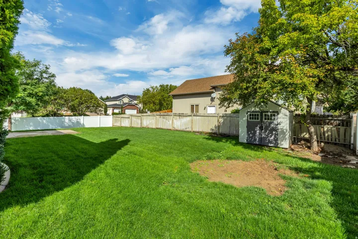 Expansive lawn area with a white vinyl fence, wood fence, mature trees, and a detached storage shed with double doors