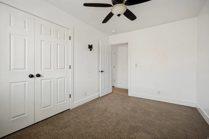 Carpeted flooring with white trim, white paneled doors, and a ceiling fan with integrated lighting