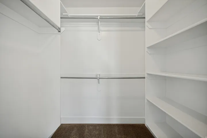 Walk-in closet featuring white walls, integrated shelving, and metal hanging rods