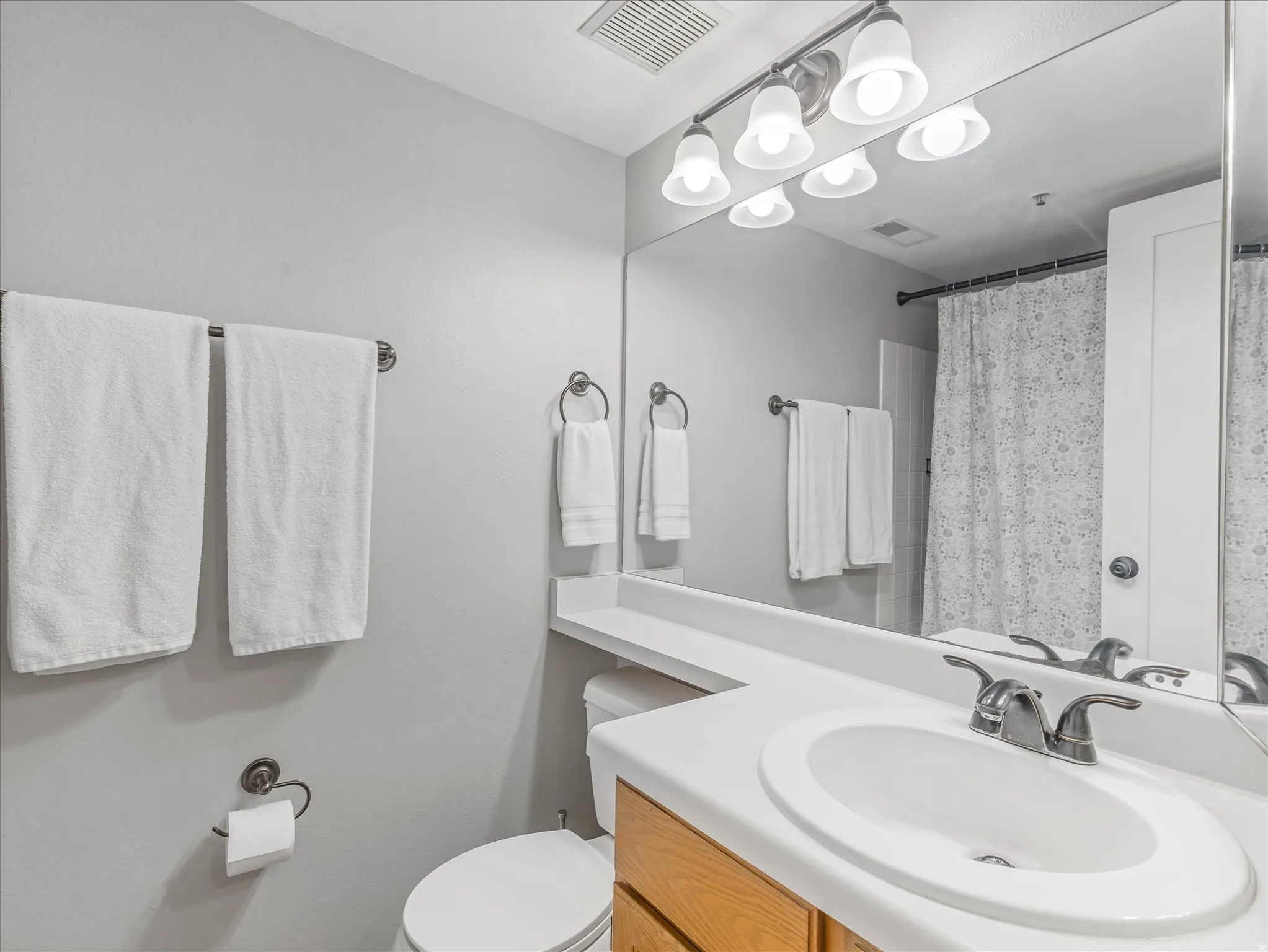 Single vanity with an integrated sink, brushed nickel faucet, wood-finish cabinetry, and a full-width mirror