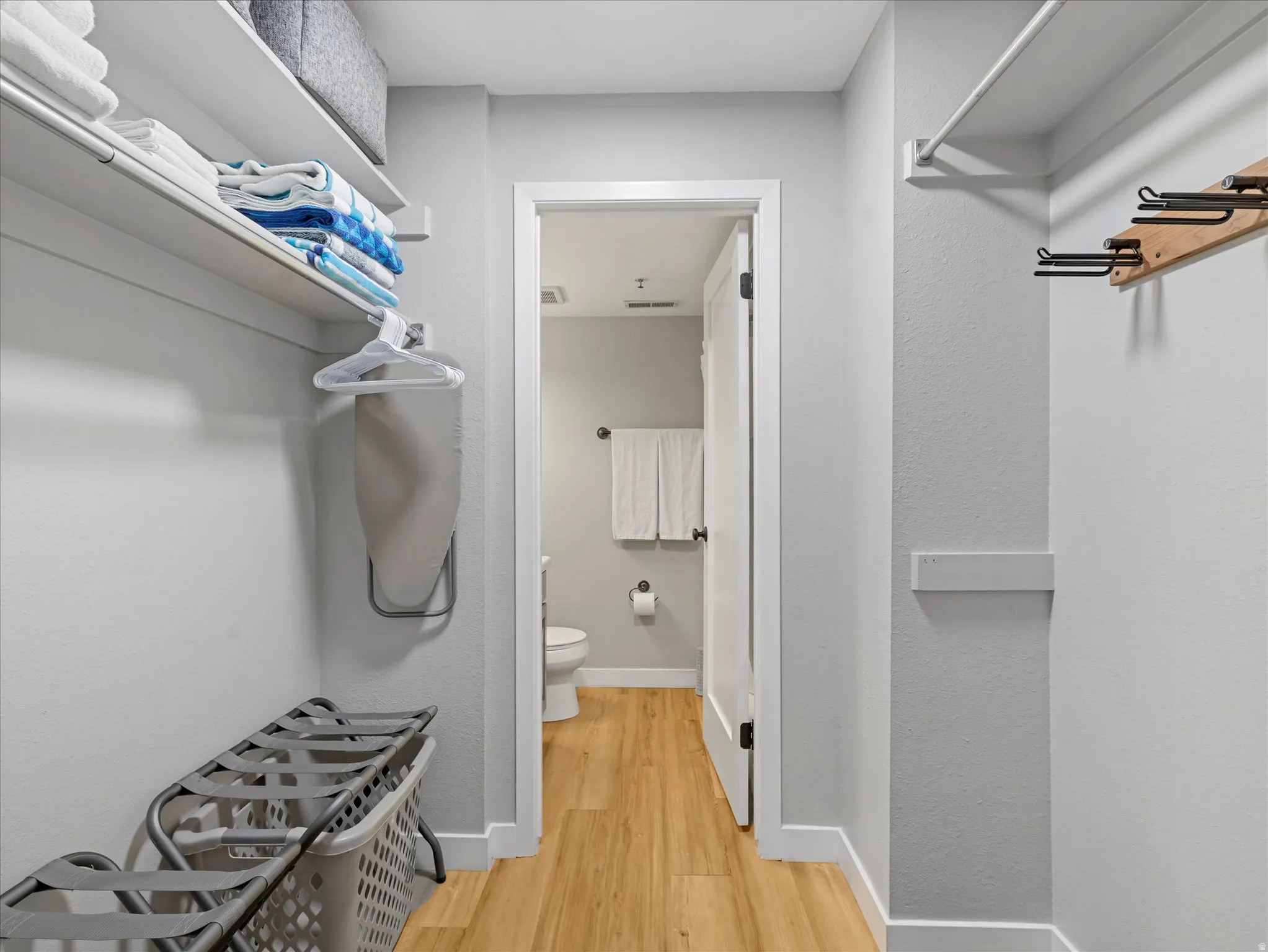 Dedicated utility space with built-in shelving, hanging rods, and wood-finish flooring