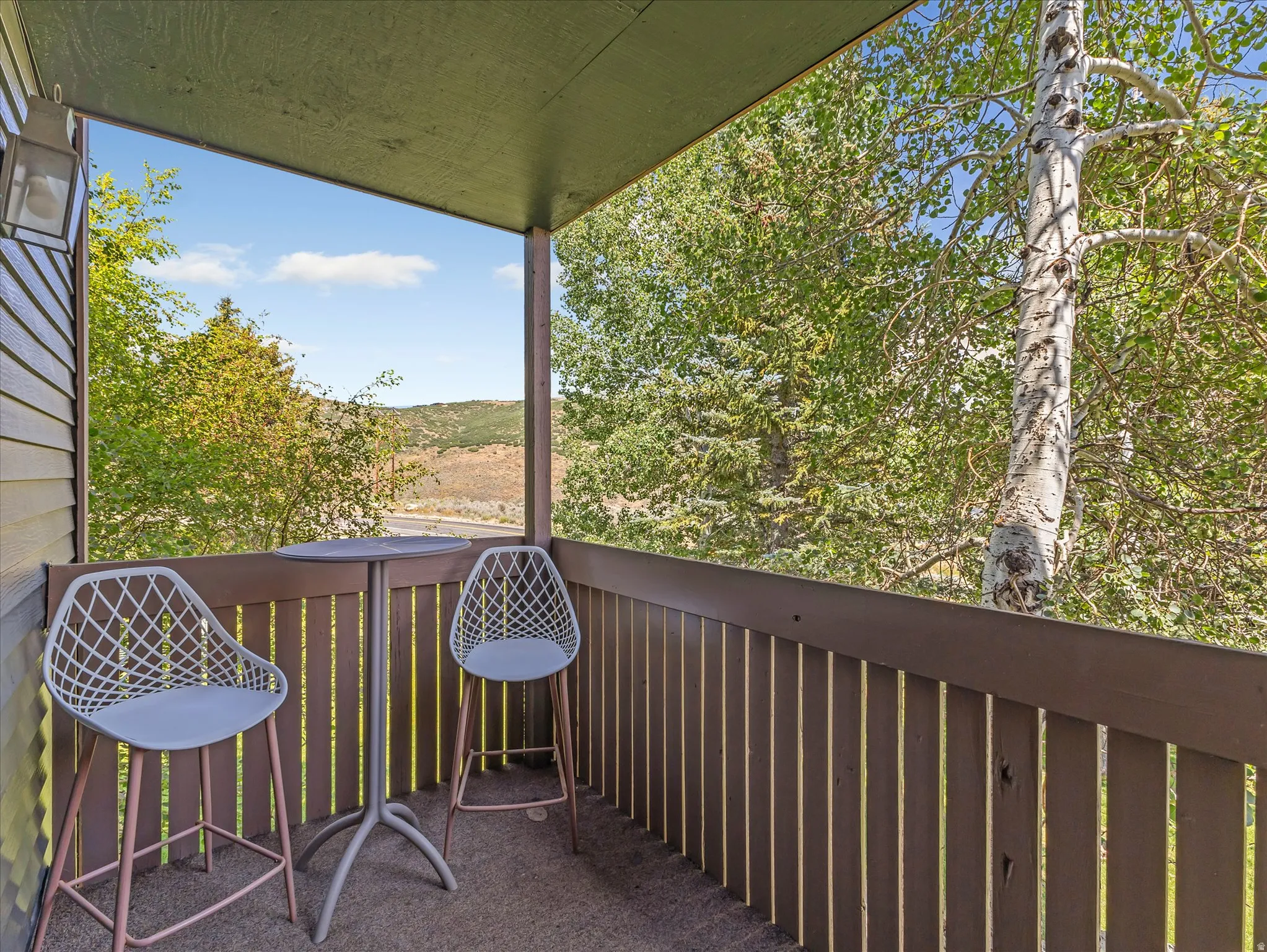 Covered outdoor balcony with a wood-slat railing, featuring an exterior wall light fixture
