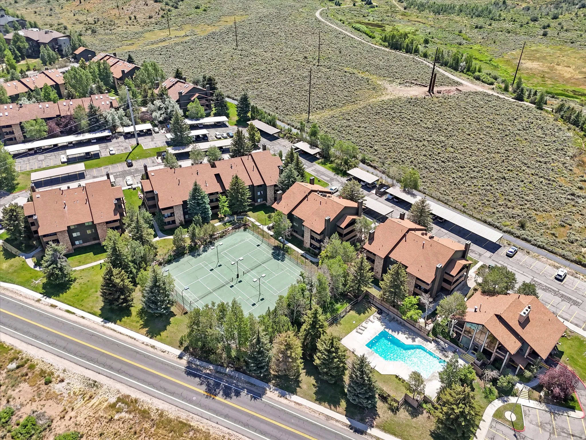 Multiple residential buildings with brown roofs, a tennis court, a swimming pool, and covered parking structures