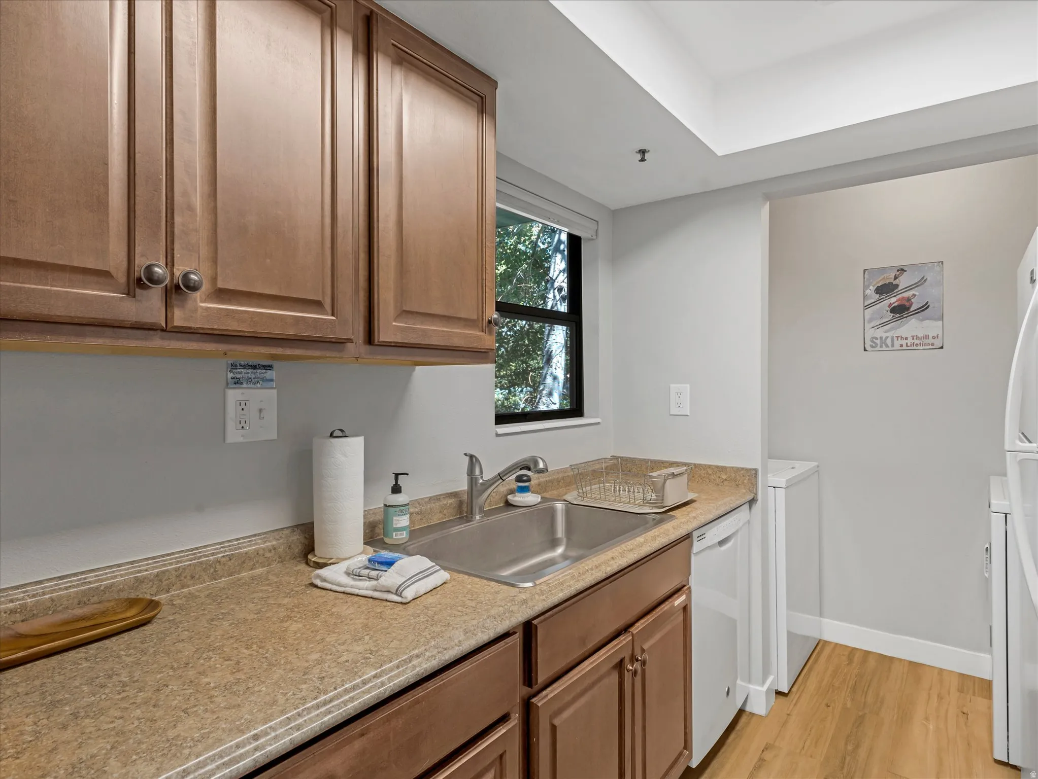 Wood-finish cabinetry with dark hardware, brown laminate countertops, stainless steel sink with chrome faucet, integrated dishwasher, and wood-finish flooring