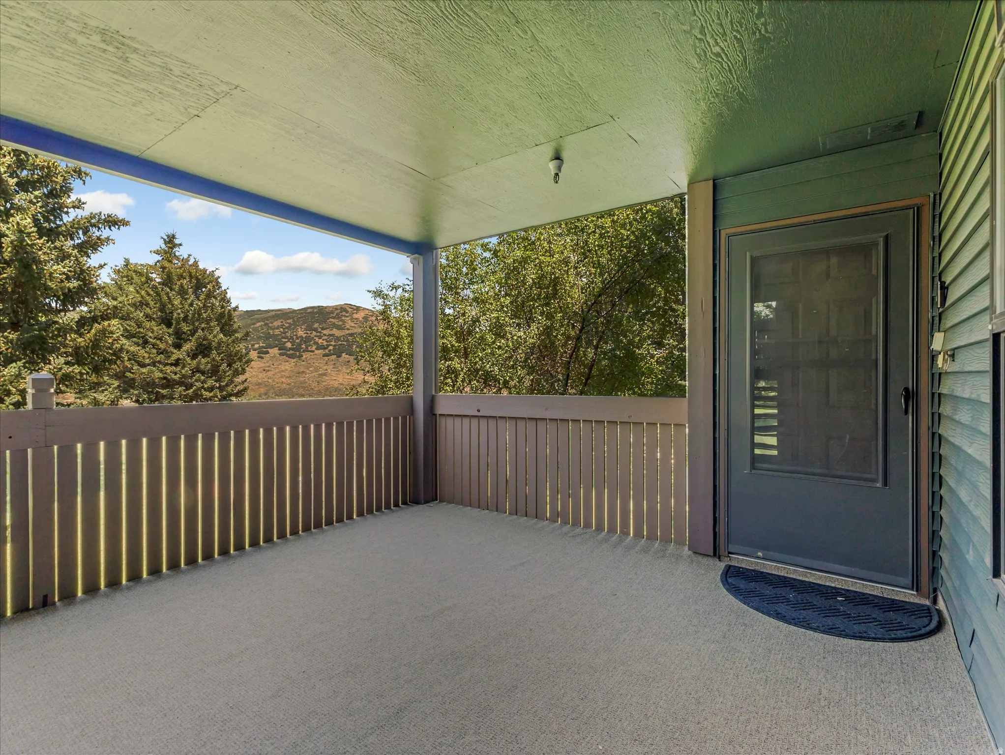 Covered porch with a textured floor, slatted wood railing, and a screen door entry