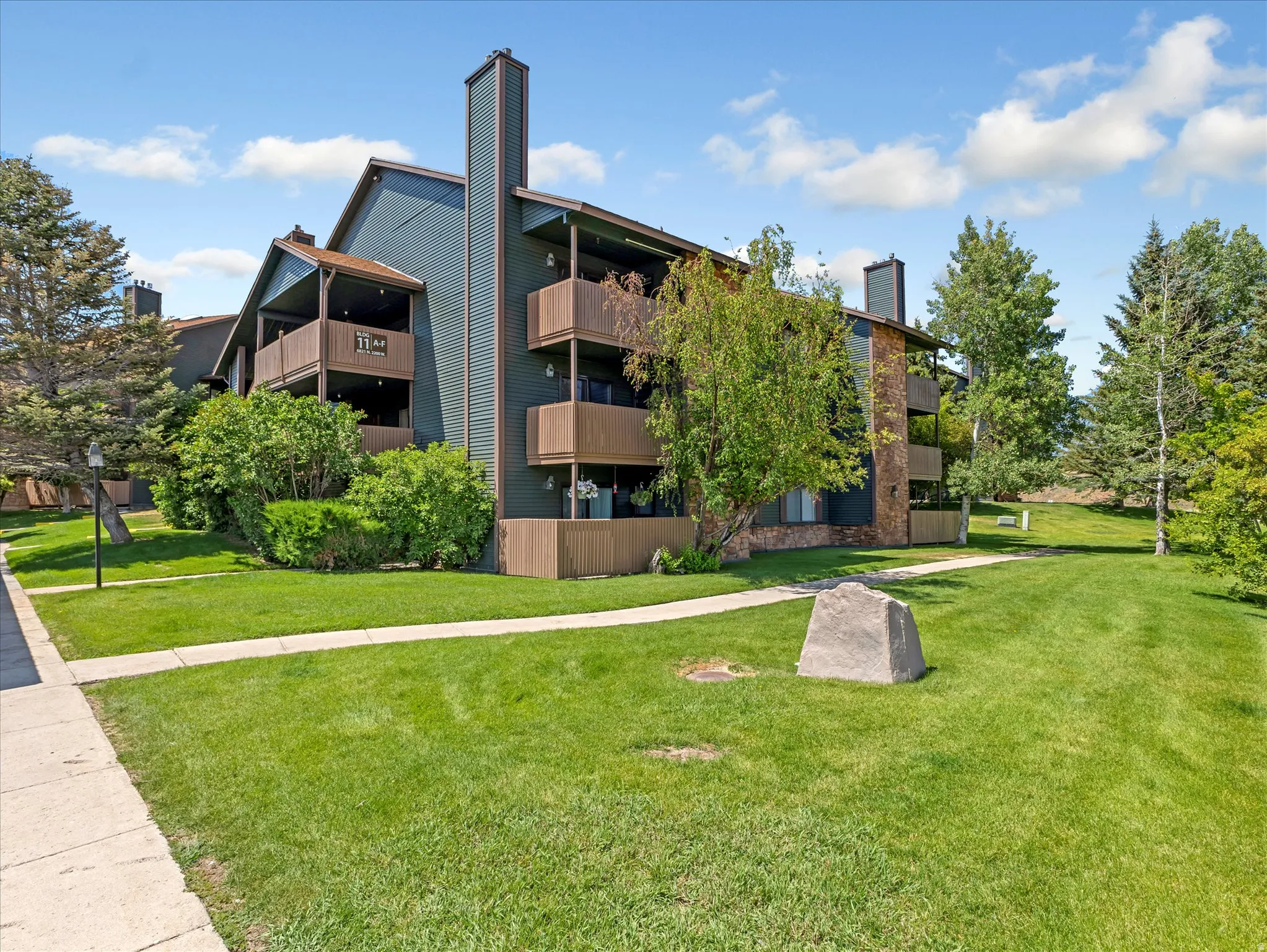 Building exterior with multiple balconies, stone veneer accents, and mature landscaping