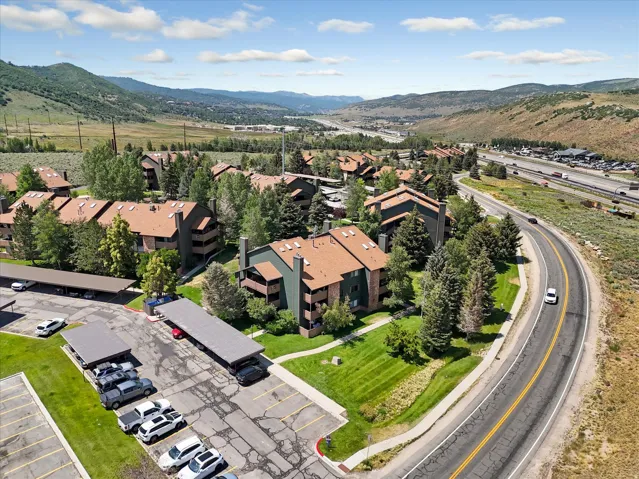 Multiple multi-story buildings with pitched roofs, surrounded by mature trees, paved parking areas with covered spaces, and a winding road