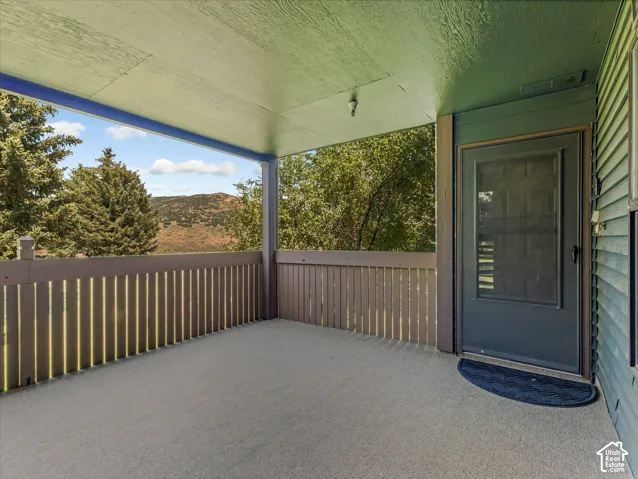 Covered porch with a textured floor, slatted wood railing, and a screen door entry