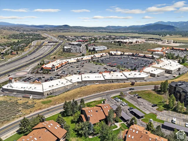 Aerial perspective showcasing a retail complex with extensive parking, adjacent to a multi-lane highway system, and surrounded by mountainous terrain