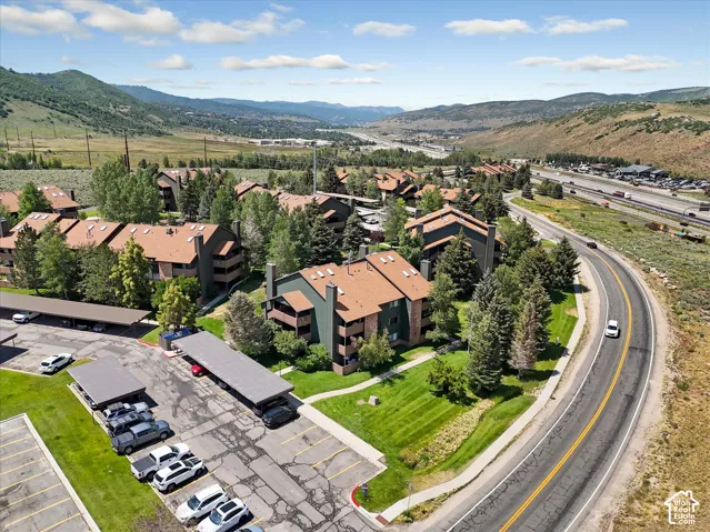 Multiple multi-story buildings with pitched roofs, surrounded by mature trees, paved parking areas with covered spaces, and a winding road