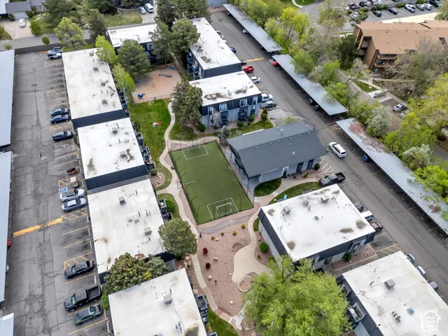 Residential buildings with flat roofs, multiple parking areas, a central green space, an artificial turf sports court, and an additional detached structure with a dark roof