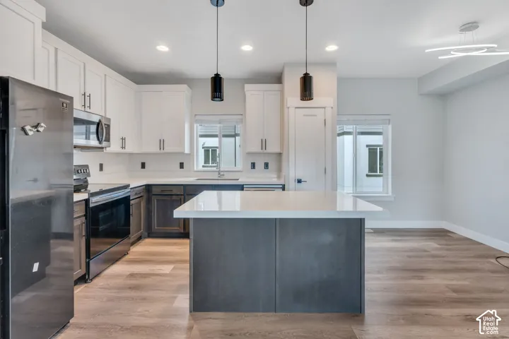 Modern kitchen featuring white upper cabinetry, dark lower cabinetry, and a central island with a light-toned countertop