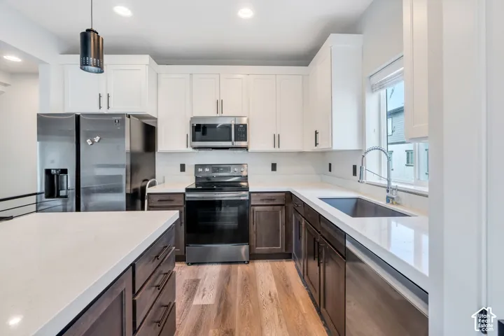 Kitchen featuring stainless steel appliances, wood-finish flooring, two-tone cabinetry, light-toned countertops, and recessed lighting