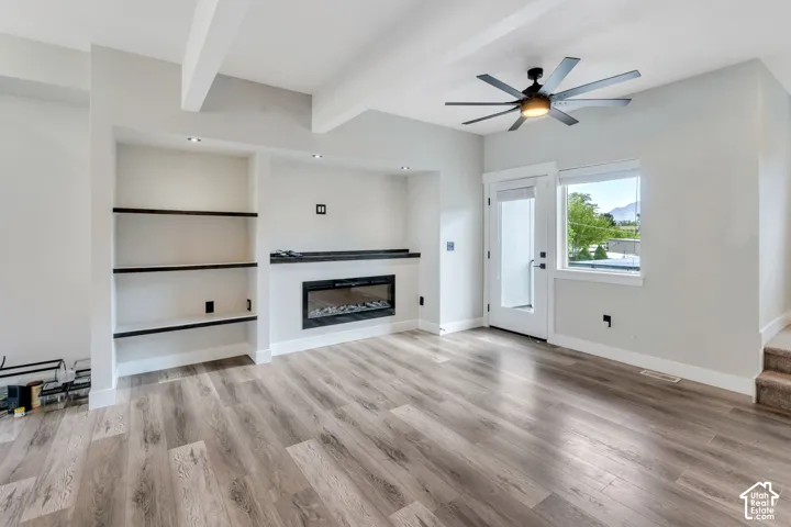 Wood-finish flooring, built-in shelving, electric fireplace, modern ceiling fan, and white trim