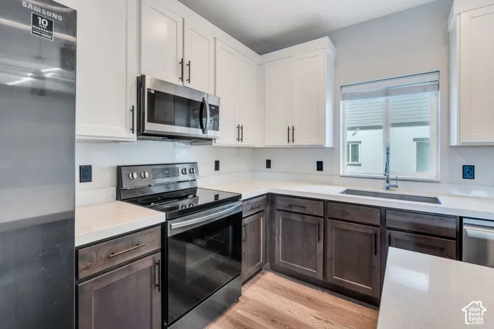 Modern kitchen featuring white shaker upper cabinetry and dark wood-finish lower cabinetry, light-toned countertops, and a stainless steel appliance suite