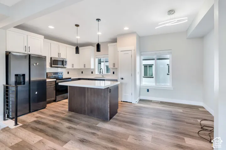 Open-concept kitchen and dining area featuring white shaker cabinetry, stainless steel appliances, and wood-finish flooring