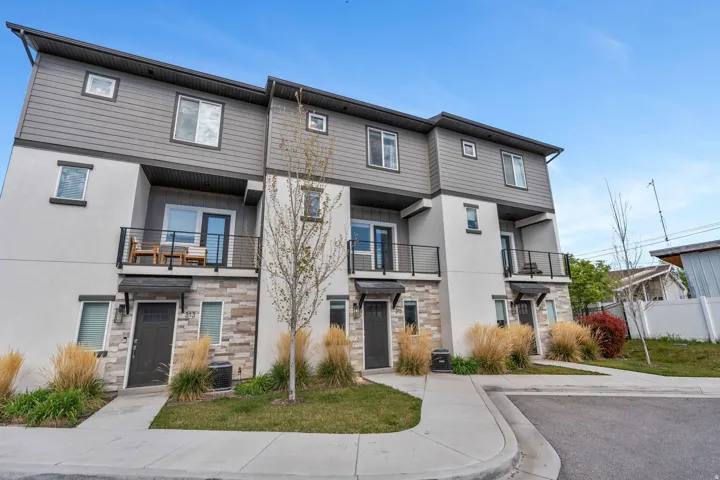 Contemporary townhome exterior featuring multi-toned siding, stone veneer accents, individual balconies with black railings, and a concrete walkway