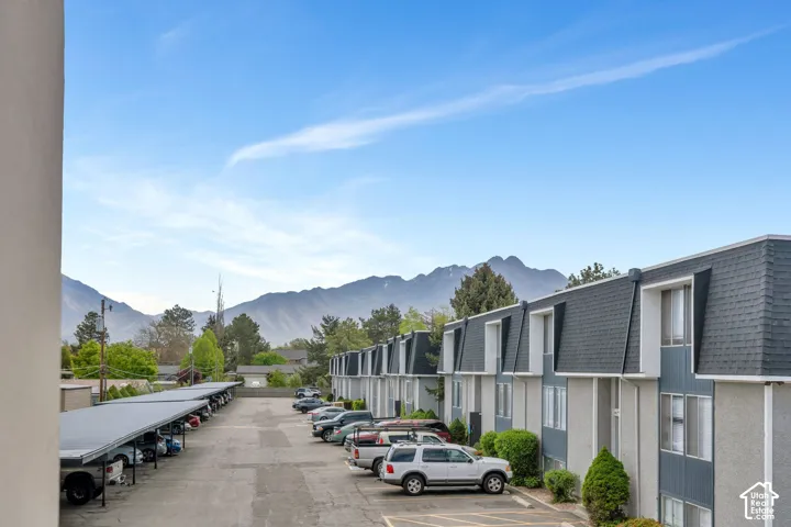 Mountain range backdrop, residential buildings with gray siding, dark shingle roofs, carport structure, paved parking area