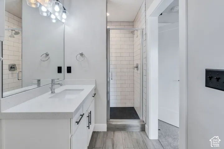 White vanity with a light-toned countertop, a shower featuring subway tile, wood-finish flooring, and a glass-enclosed shower