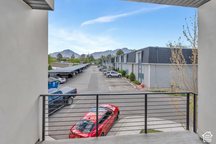 Balcony with contemporary horizontal bar railing, overlooking covered parking, paved parking lot, and distant mountains
