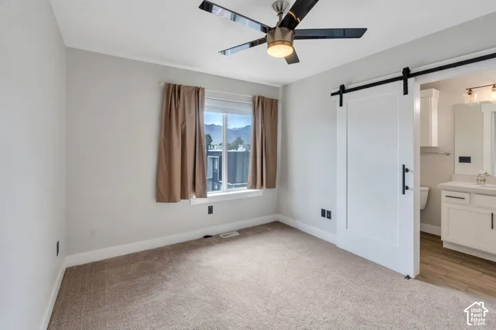Carpeted room with a ceiling fan, a window, and a white barn door