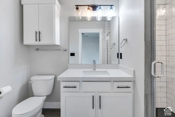 White shaker-style cabinetry with matte black hardware, white countertop, rectangular undermount sink, and a glass-enclosed shower with subway tile