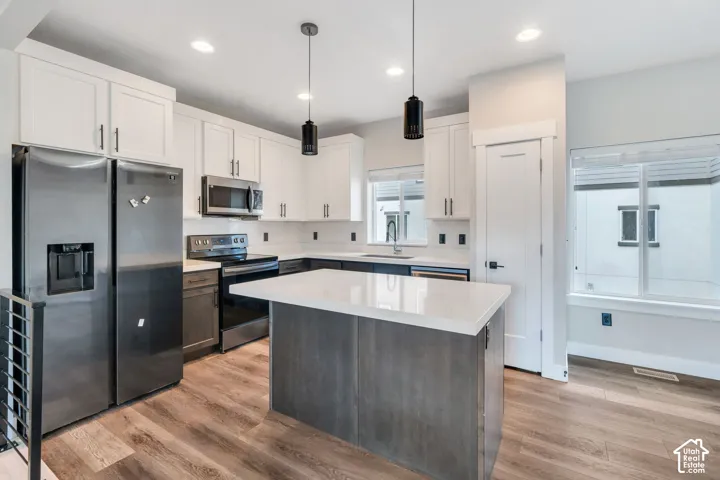 Kitchen featuring stainless steel appliances, white cabinetry, a center island with a light-colored countertop, wood-finish flooring, and pendant lighting