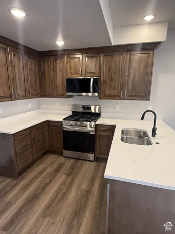 U-shaped kitchen featuring wood-finish cabinetry, light-toned countertops, wood-finish flooring, stainless steel range, and stainless steel microwave