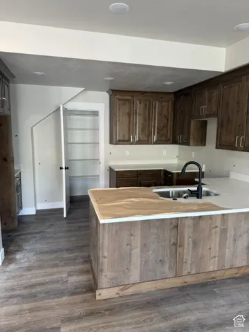 Kitchen featuring recessed lighting, wood-finish flooring, wood cabinetry, a center island with a sink, and a pantry with built-in shelving