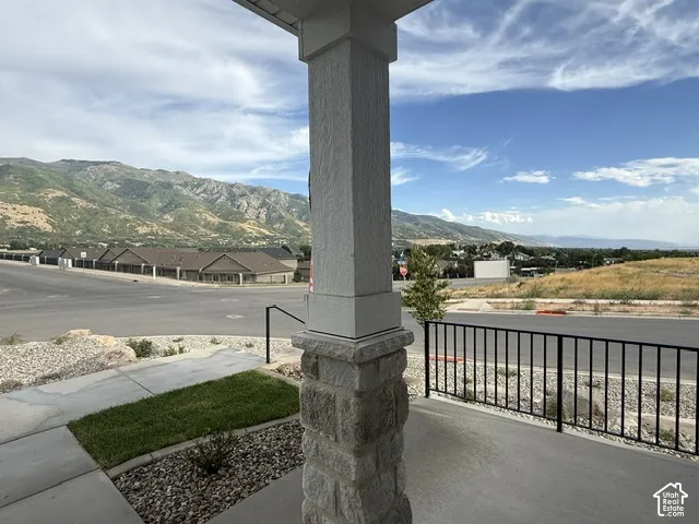 Stone-clad porch column with a black metal railing, offering a mountain backdrop and a partial streetscape