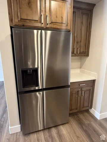 Stainless steel refrigerator, upper and lower wood cabinetry, light-toned countertop, and wood-finish flooring