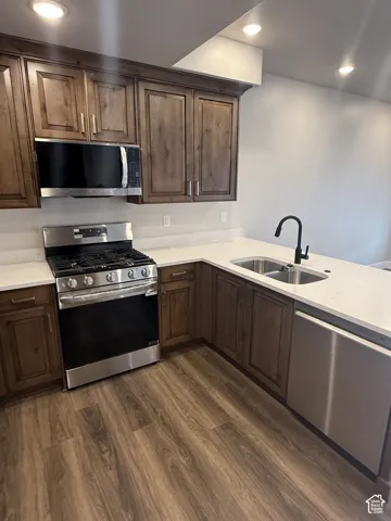 Wood-finish flooring, stainless steel appliances, white countertops, dark wood cabinetry, and a double basin sink
