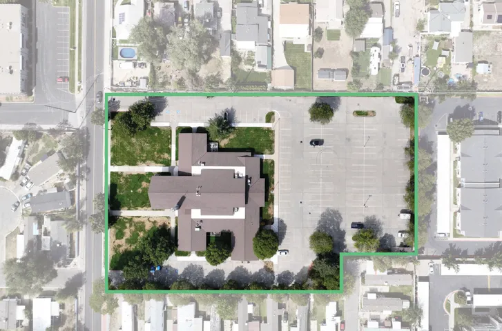 Expansive property featuring a large structure with multiple wings, abundant paved parking, green spaces, and mature perimeter trees