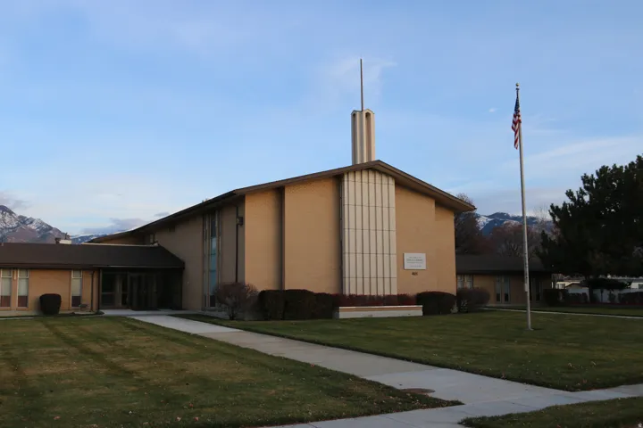 Brick exterior building with prominent steeple and an expansive lawn, featuring mature shrubbery and a concrete walkway
